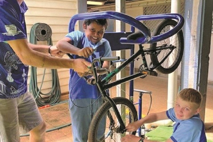 Malanda State School teacher aide Tim Barker, Raymond Mathieson and Ryan Coe restoring bikes to ride to school every morning.