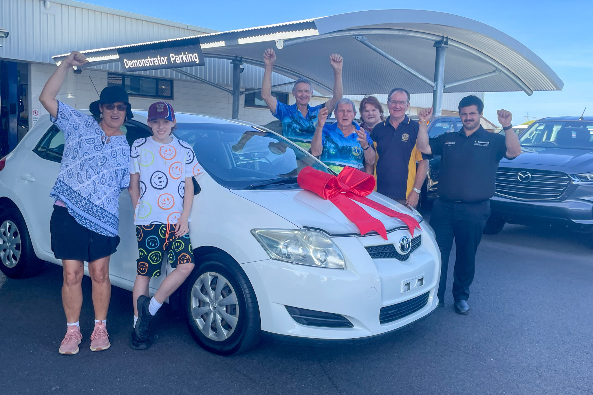 Phillippa McLean and her son Darcy (front) with Mareeba Lions Club and Rotary club members and Mareeba Mazda staff with her new car.