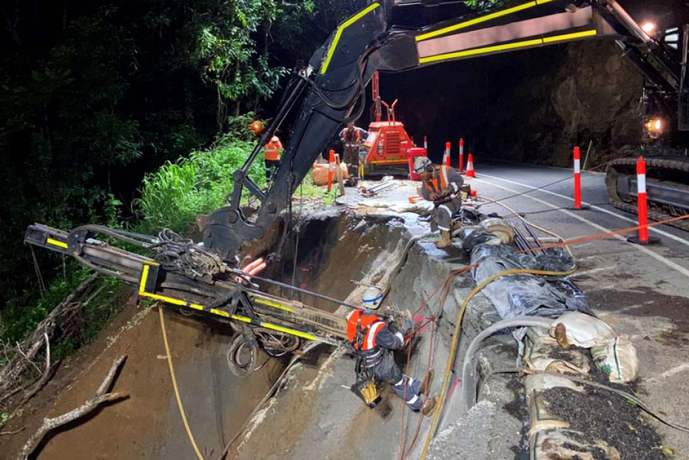 Transport and Main Roads crew abseiling off the side of an excavator in the middle of the night on the Kuranda Range Road as they try to repair December’s damage.