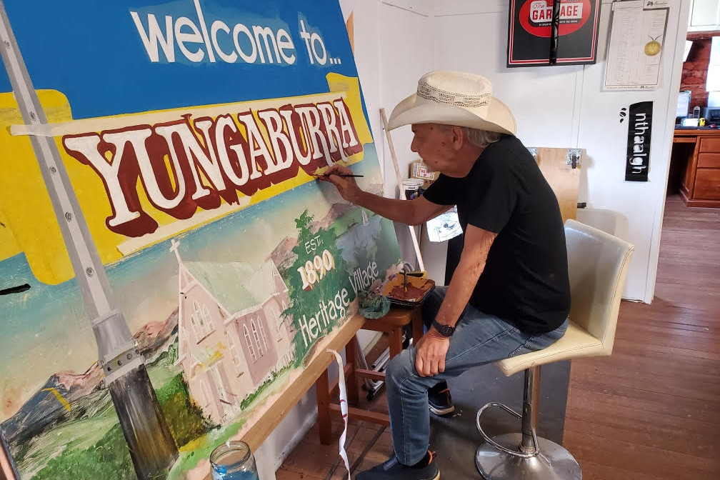 Accomplished artist Ian Waldron is refreshing Yungaburra’s welcome signs which he painted 20 years ago.